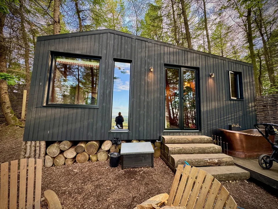 The dark wooden cabin set into the Yorkshire hillside, its wide deck and full-height windows facing the valley below.