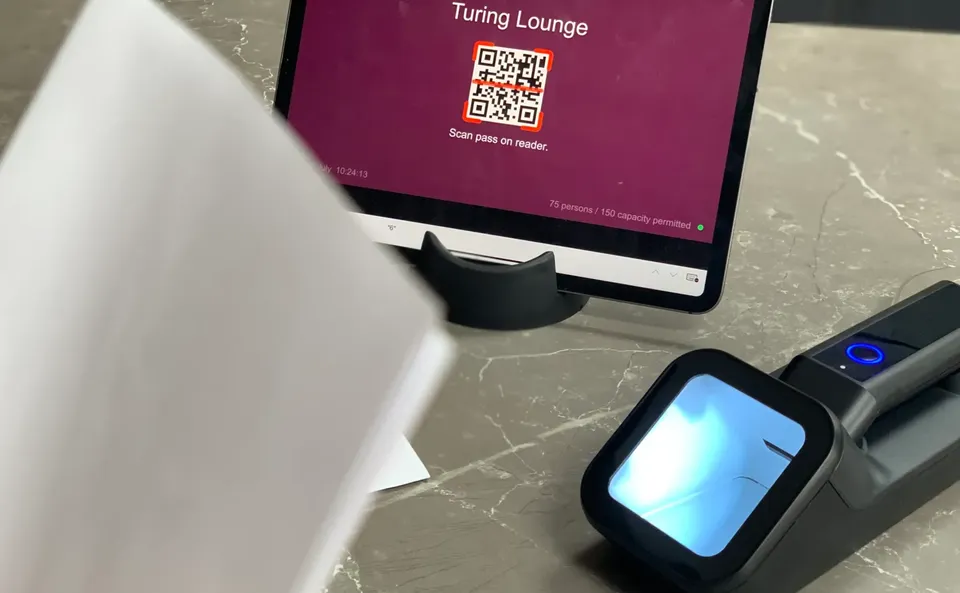 A Power Apps event entry control kiosk on an iPad, with a docked Alacrity barcode scanner ready on a stand for attendees to tap their passes against.