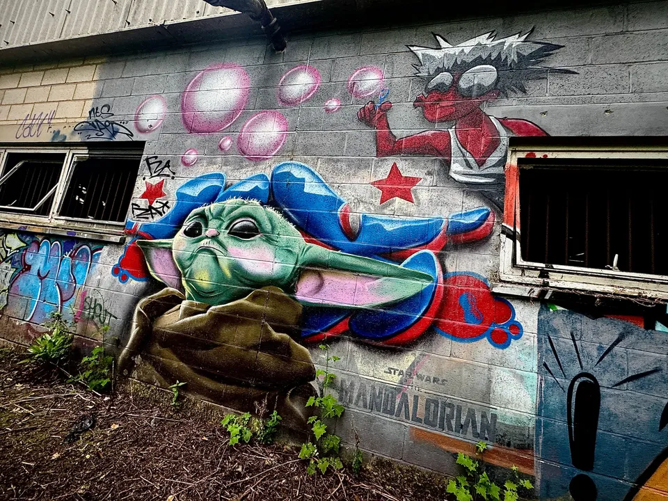 Large Baby Yoda (Grogu) street art mural painted on the exterior wall of an abandoned building.